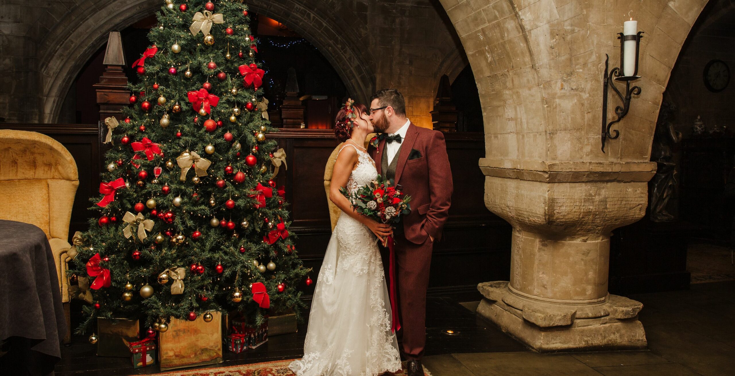 Couple kisses by a Christmas tree at their affordable wedding venue